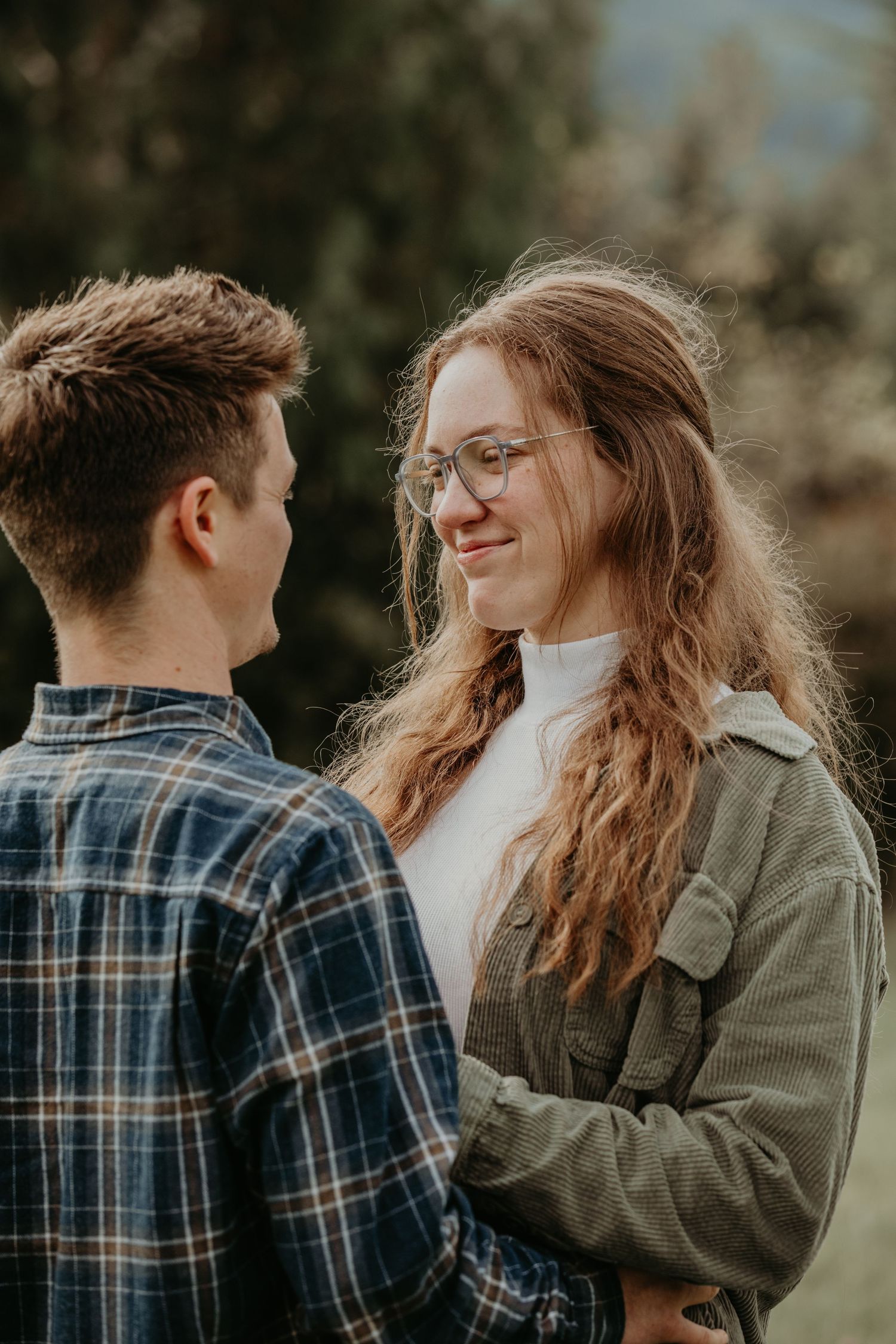 Two people in plaid and green jackets sharing an intimate moment outdoors in soft lighting.