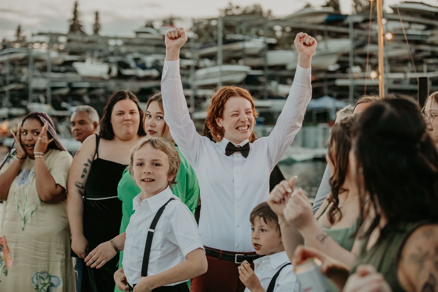 Joyful wedding guests dance and celebrate on a boat during a festive marina reception party.