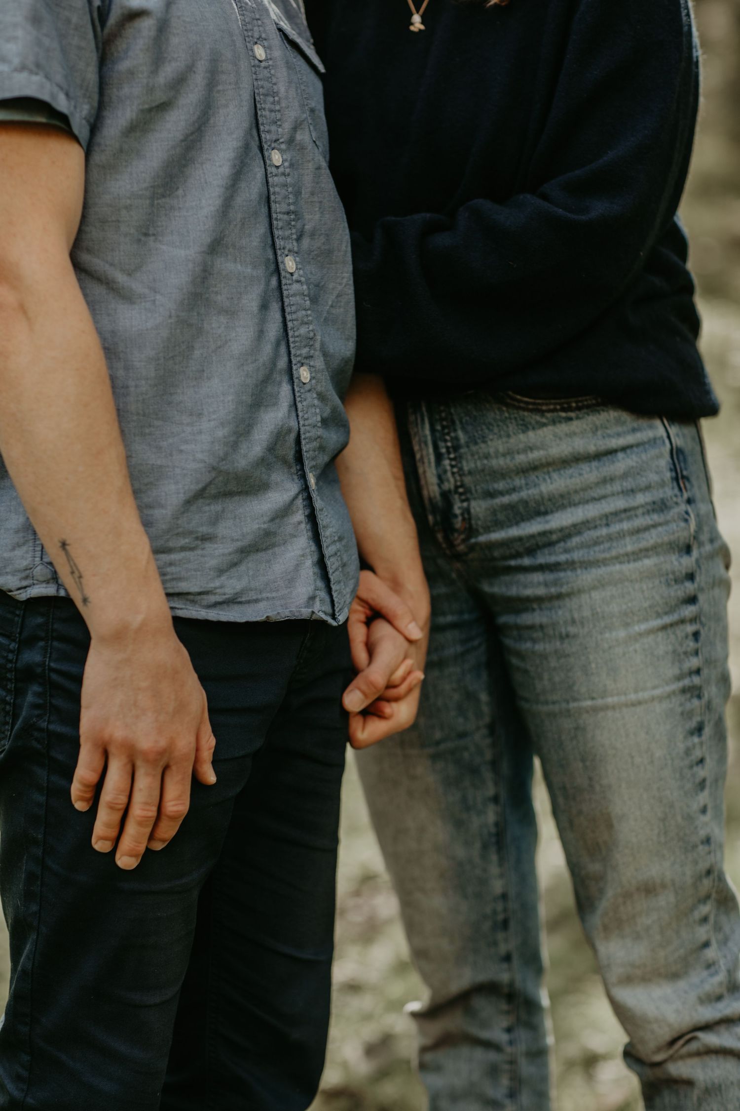 Two people in casual attire standing close together while holding hands intimately in faded jeans and shirts.