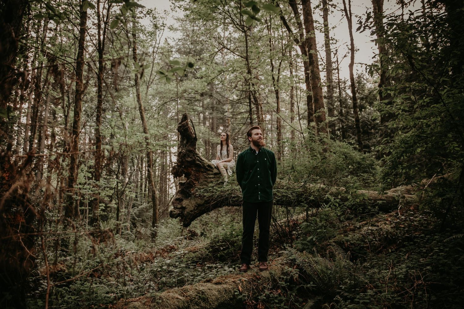 A moody forest scene with dark figures near a rock formation on an overcast day.