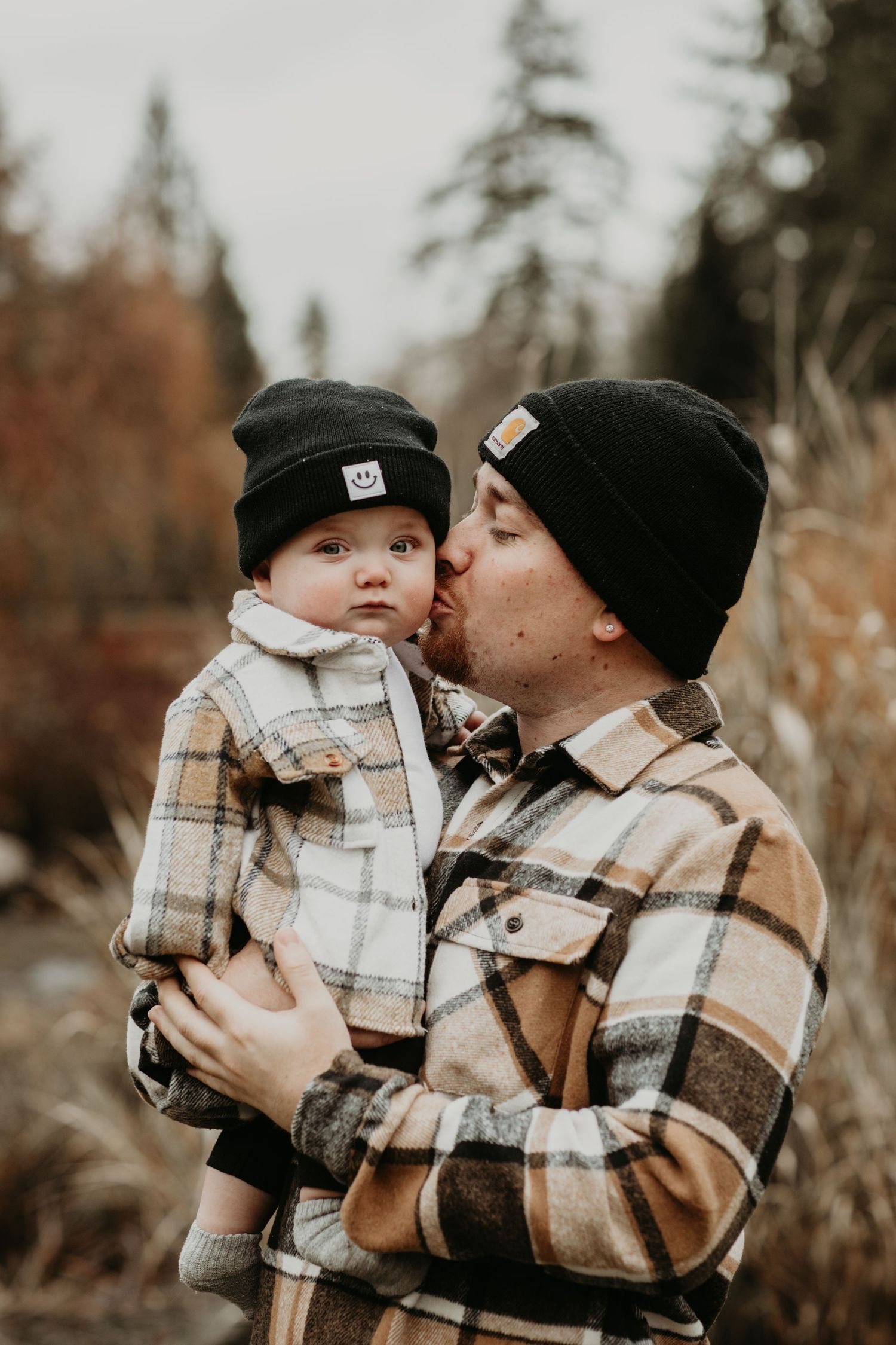 Sweet moment captured in autumn with matching plaid jackets and black beanies in a forest setting.