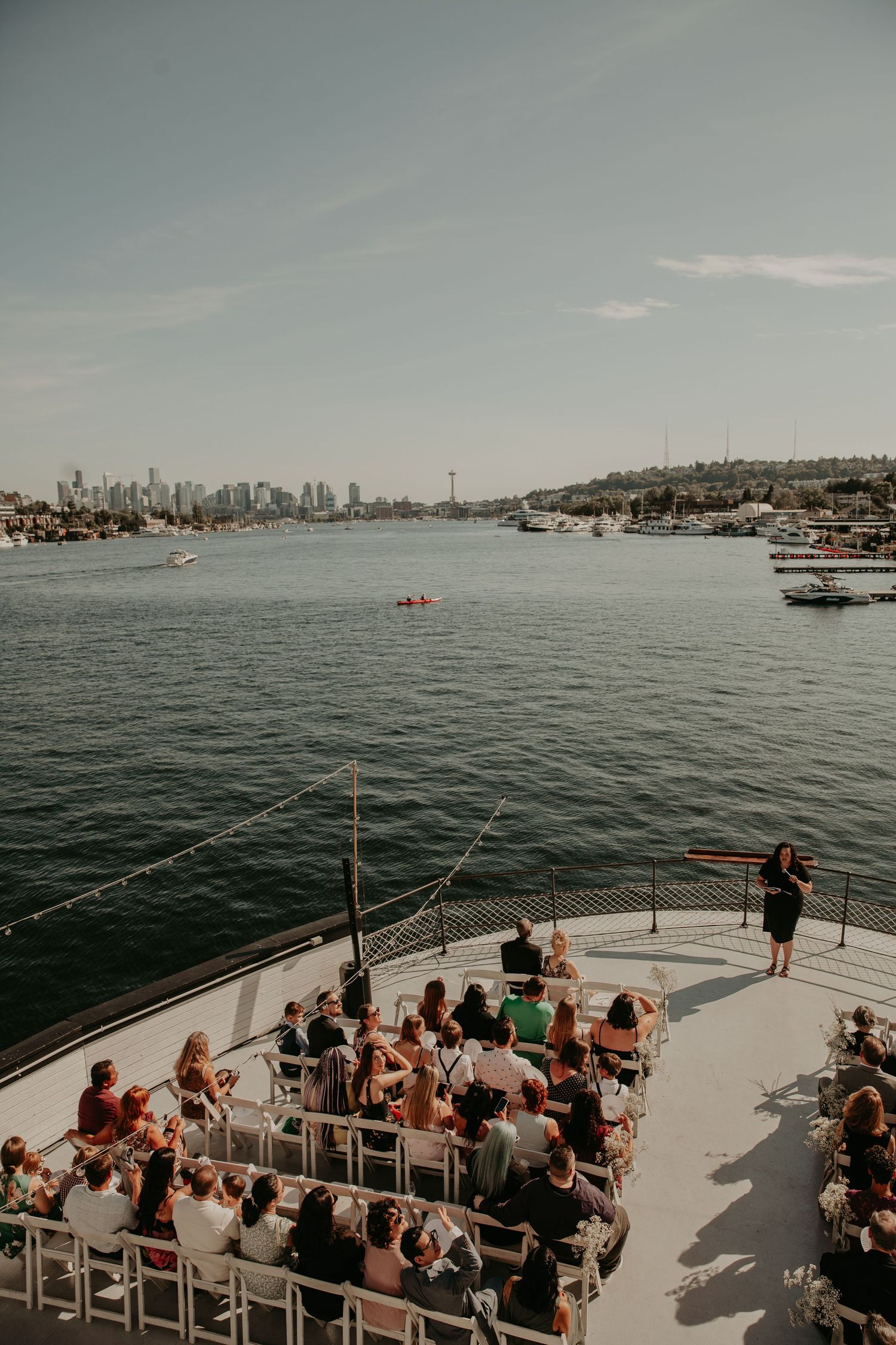A wedding ceremony takes place on a boat deck with the city skyline visible across the harbor.