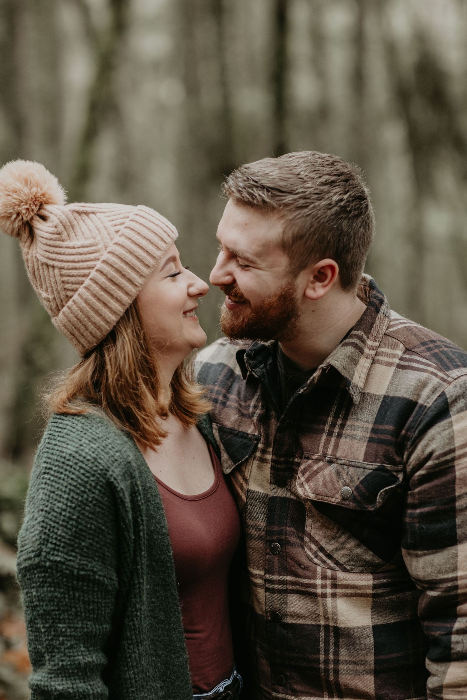 Cozy couple in winter attire share an intimate moment in a wooded setting.