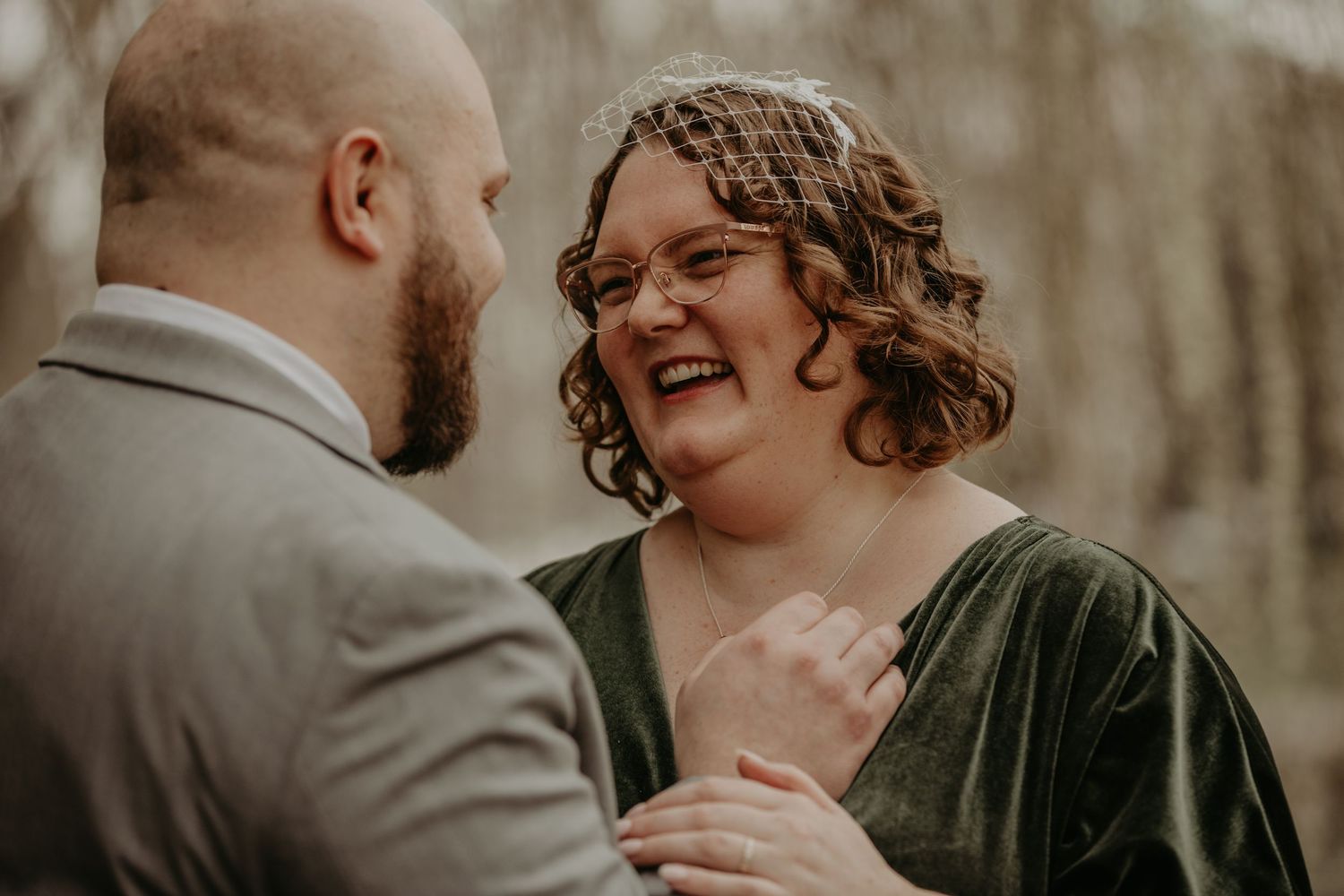 A joyful couple shares a sweet candid moment together in a forest wearing formal attire.