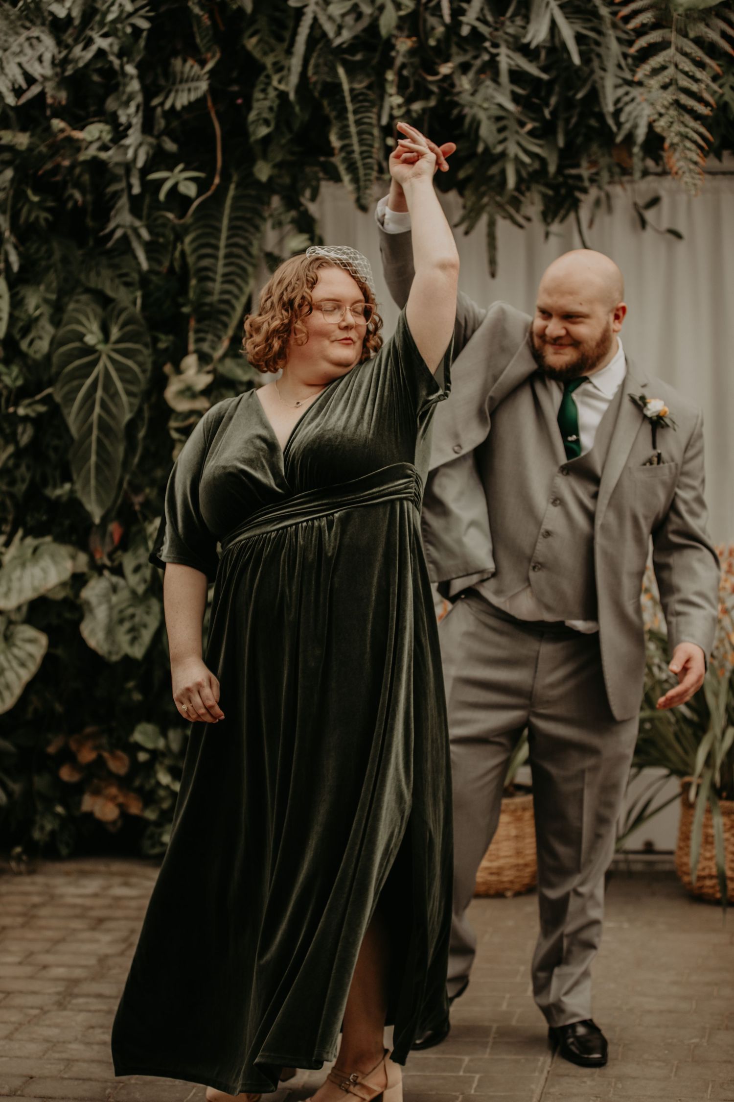 A couple celebrates joyfully in formal attire while dancing in a garden setting.