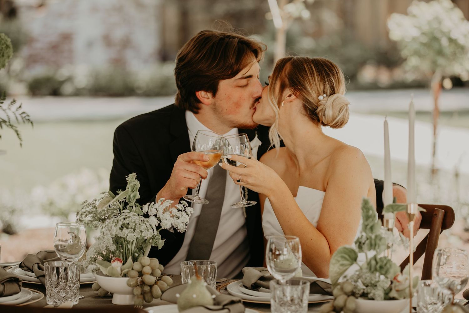 Couple shares romantic moment toasting champagne at elegant outdoor wedding reception with floral table decor.