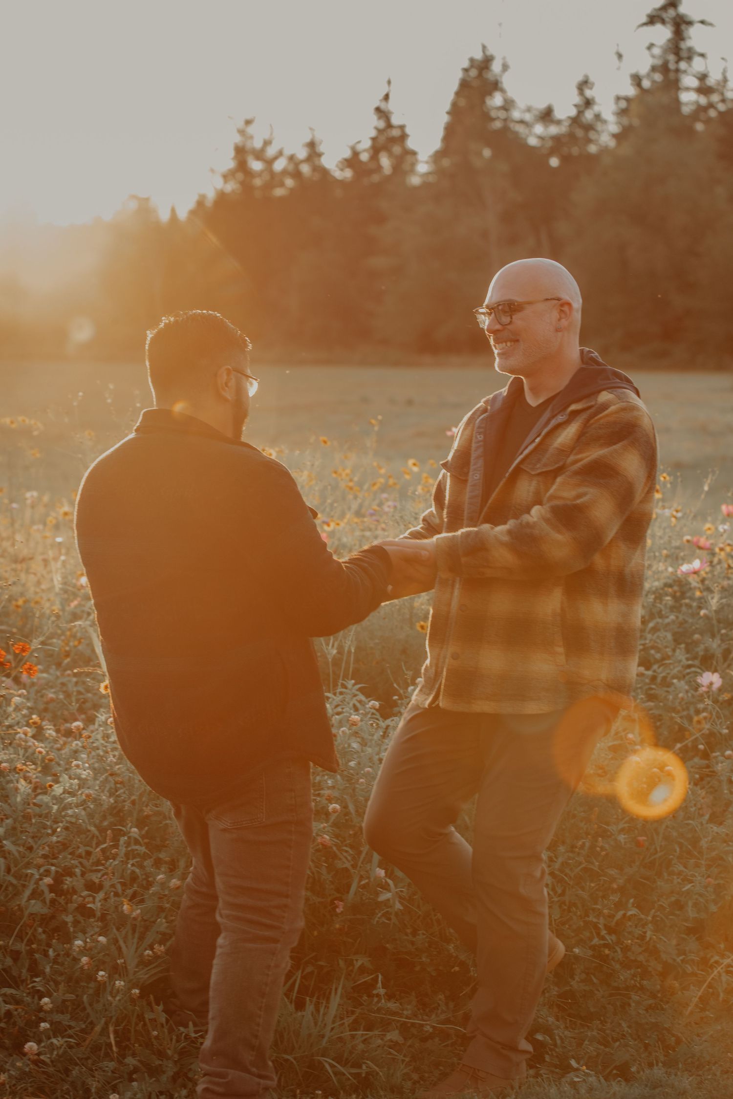 Two people share an intimate moment in a golden field at sunset wearing casual outdoor attire.