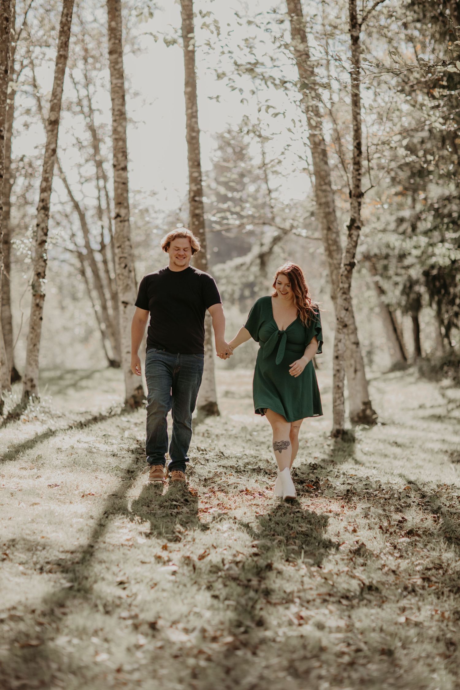 A couple walks hand in hand through a sunlit birch forest as sunlight filters through the trees in a dreamy scene.