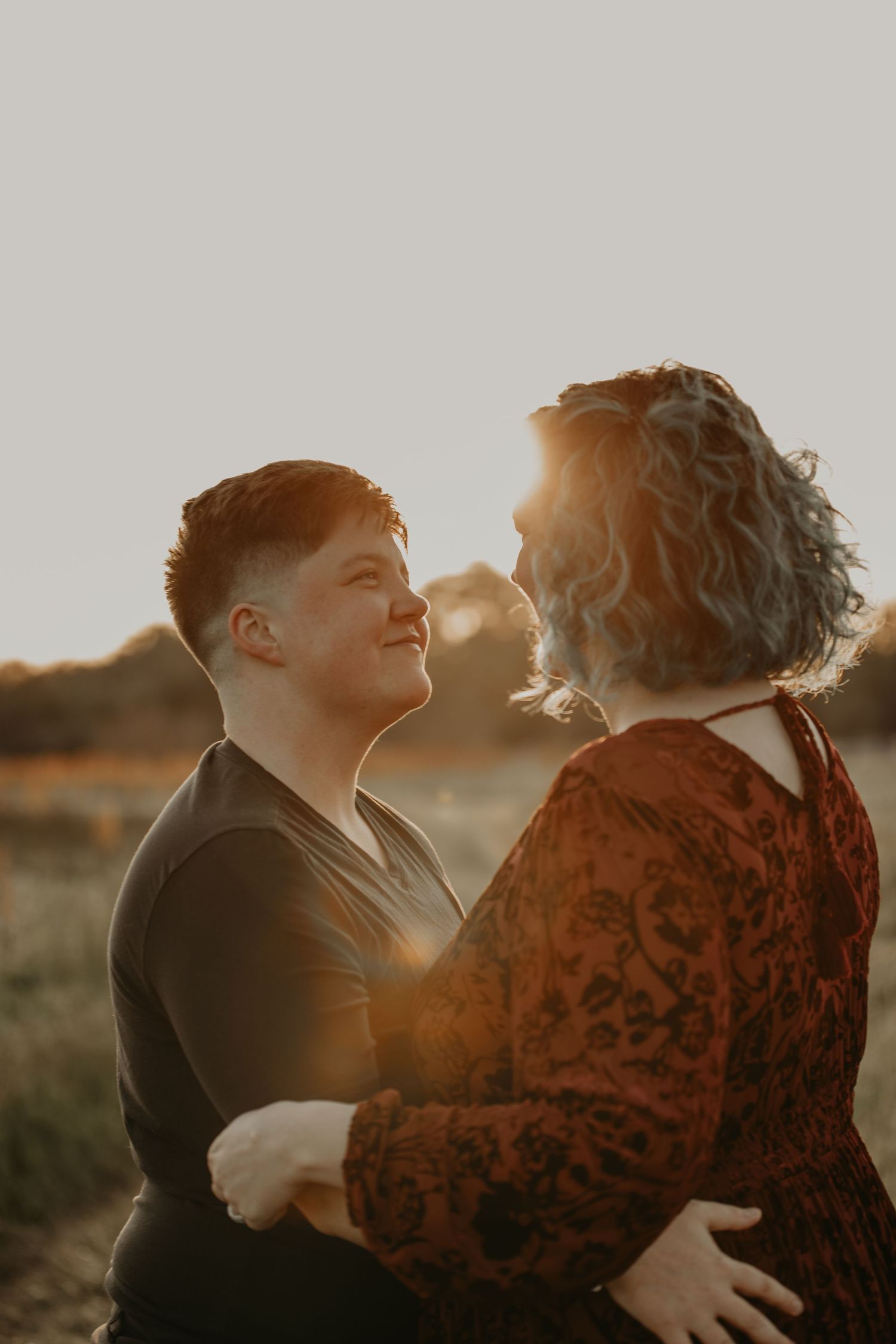 Intimate couple sharing a romantic moment in golden sunlight against a natural outdoor setting.
