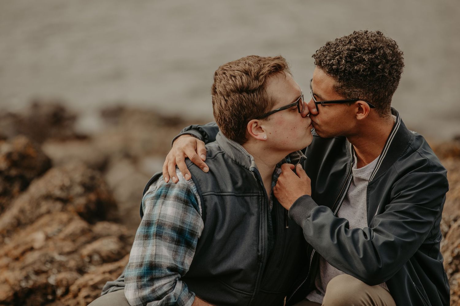 Two people sharing an intimate moment together while sitting on rocky terrain at sunset.