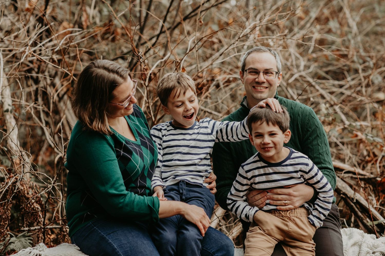 A family of four wearing green and striped outfits sits together outdoors during autumn.