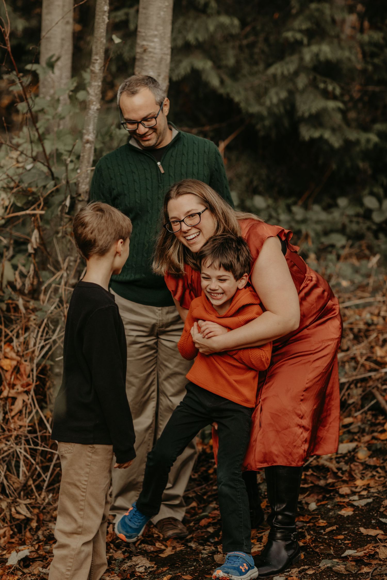 A family shares a joyful moment together in autumn woods, dressed in cozy sweaters and laughing together.