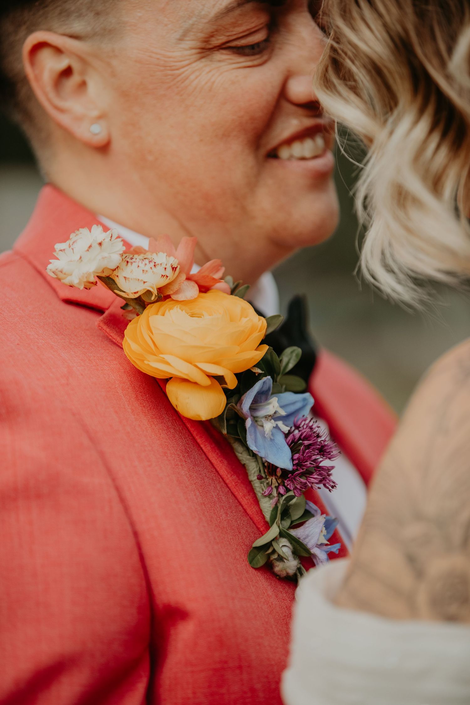 Close-up of colorful floral boutonniere with orange ranunculus and purple blooms on coral suit jacket.