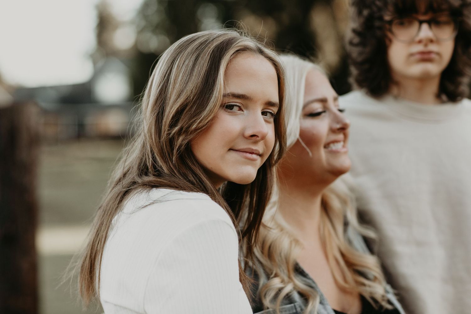Three people standing together outdoors in warm lighting with soulful expressions and casual wear.