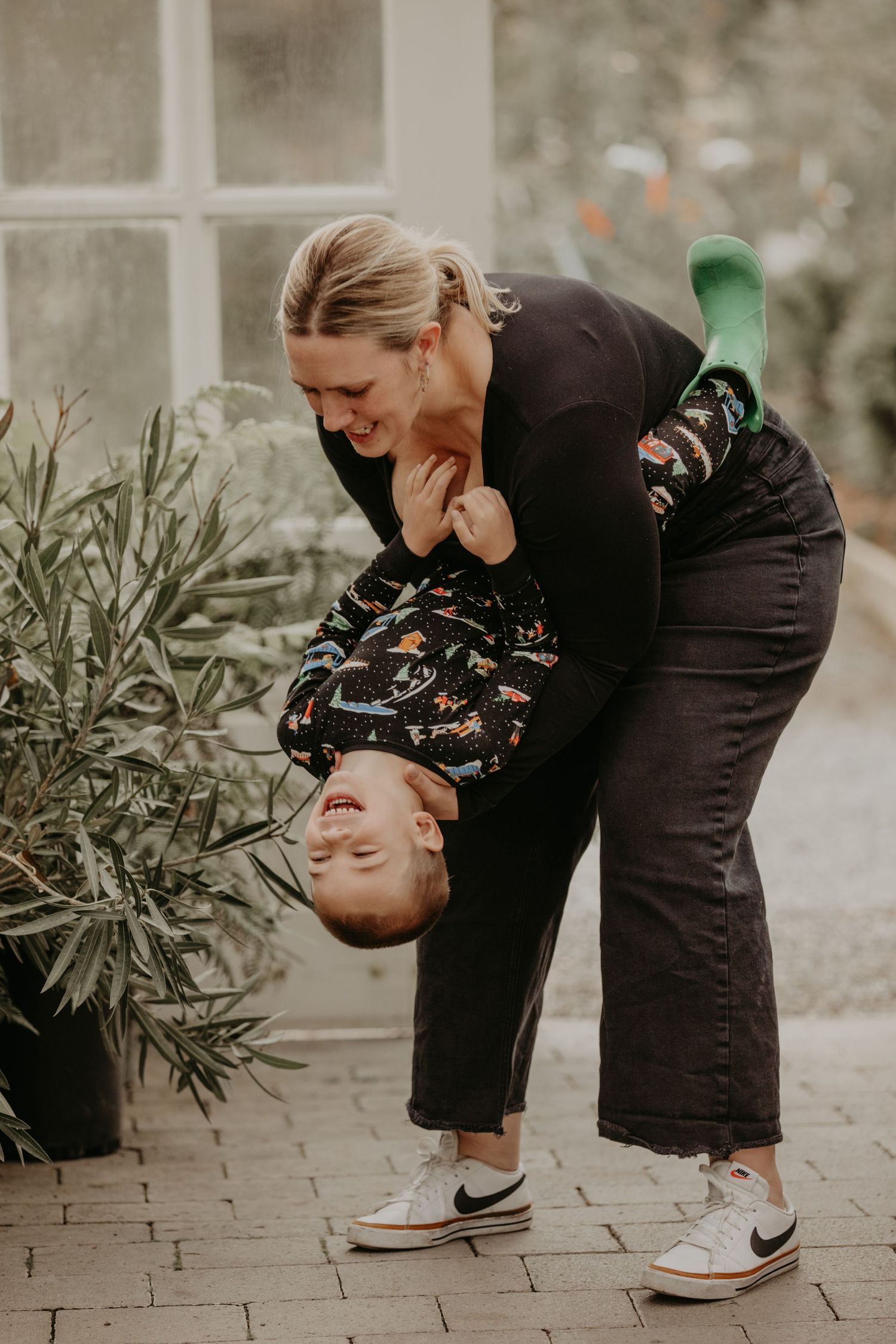 Two people in black outfits share a joyful moment while laughing together on a brick patio outdoors.