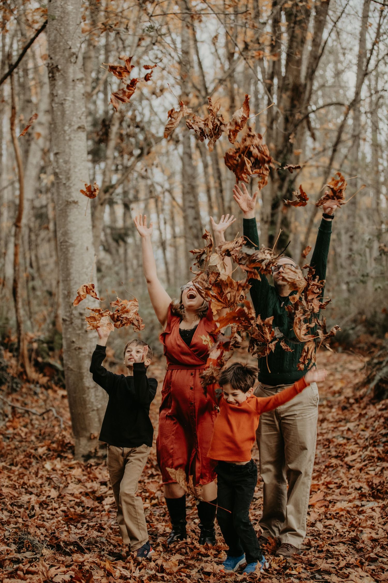 A group playfully throws autumn leaves in the air while standing in a forest filled with fallen foliage.