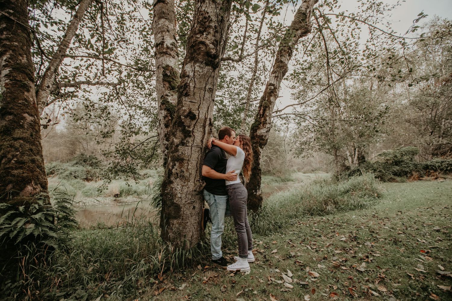 A couple embraces near birch trees in a dreamy, natural woodland setting on a misty day.