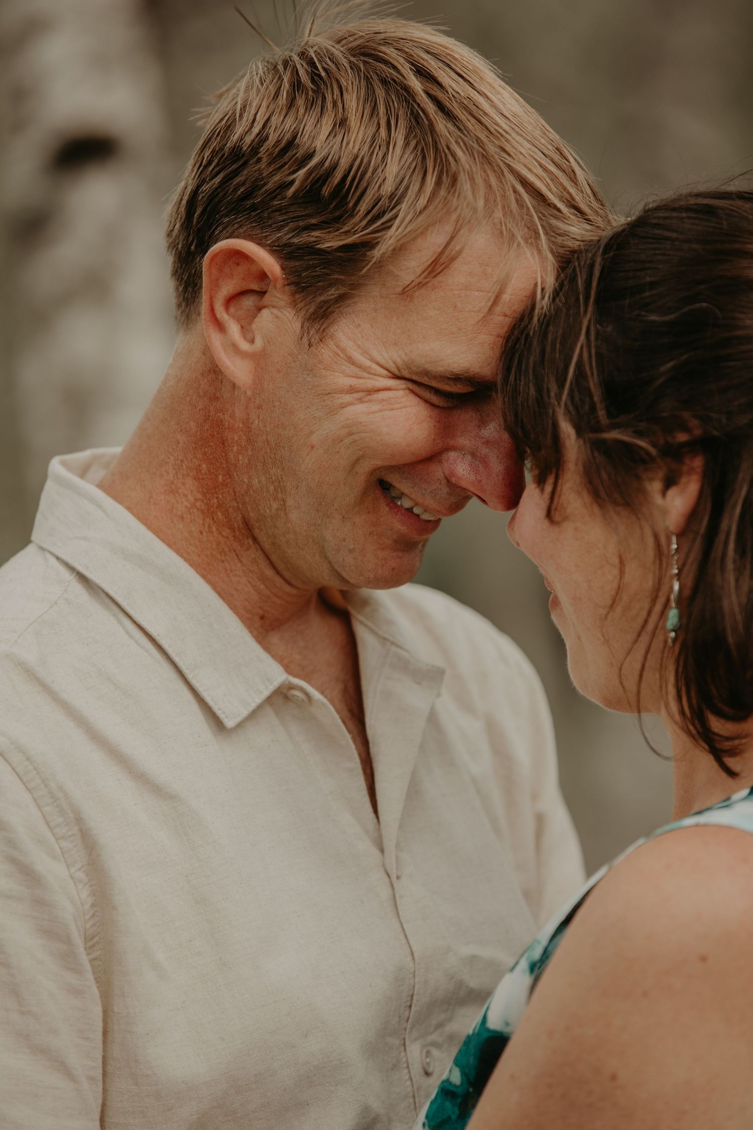 A loving couple shares an intimate moment together in natural lighting, wearing light colored clothing.
