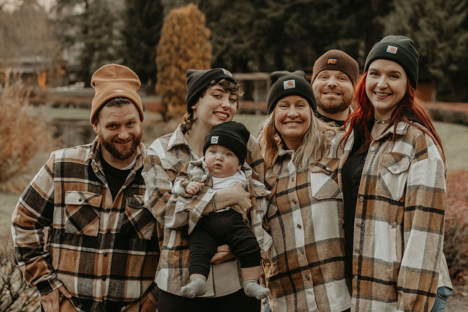 A group wearing coordinated plaid flannel jackets and beanies pose together outdoors in autumn.