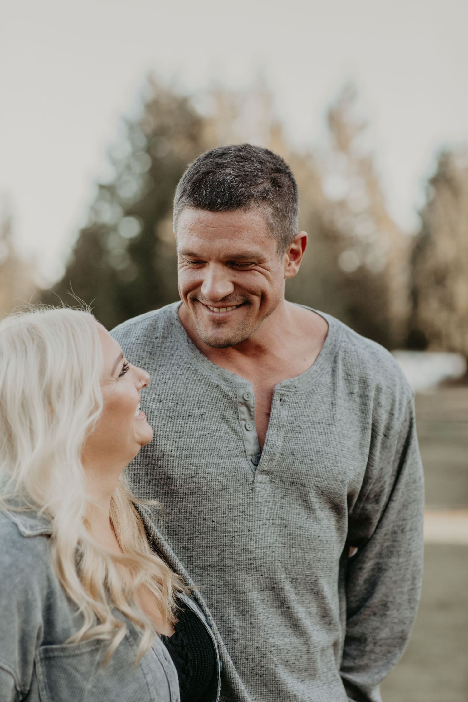A couple shares a candid laughing moment together outdoors during a casual photoshoot at sunset.