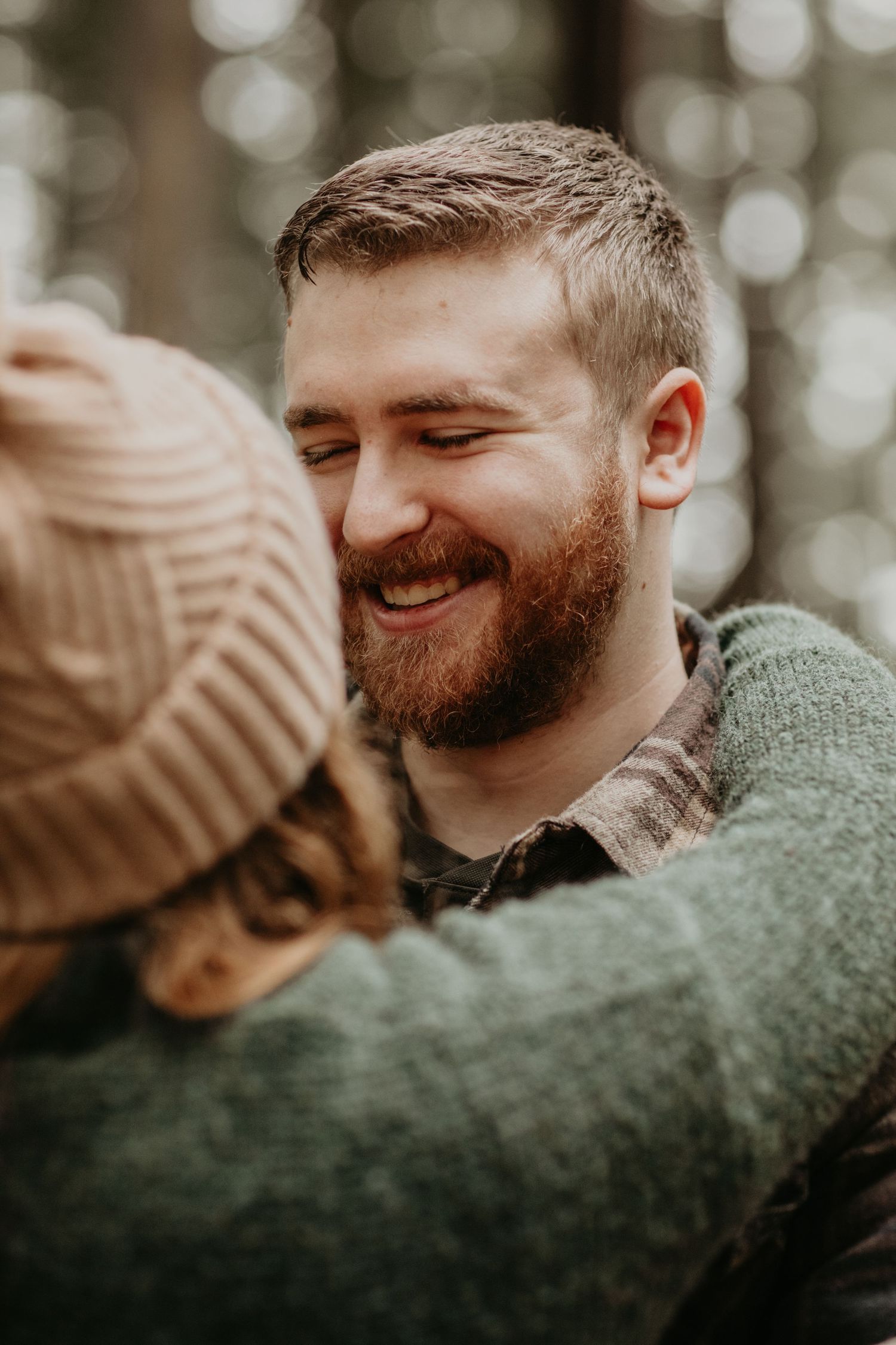 A close-up candid photo of a couple sharing an intimate moment outdoors with soft bokeh in the background.