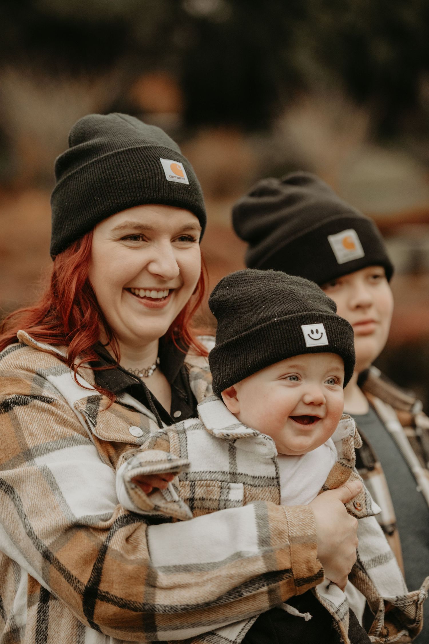 A group in matching plaid jackets and Carhartt beanies share a joyful moment together in an autumn setting.