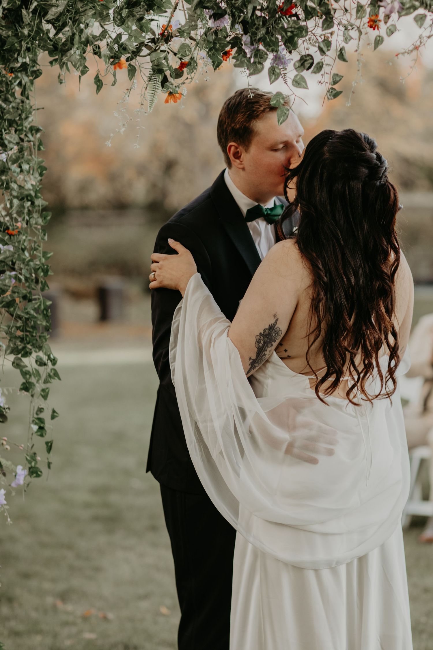 A couple shares a romantic kiss under a floral arch during their wedding celebration.