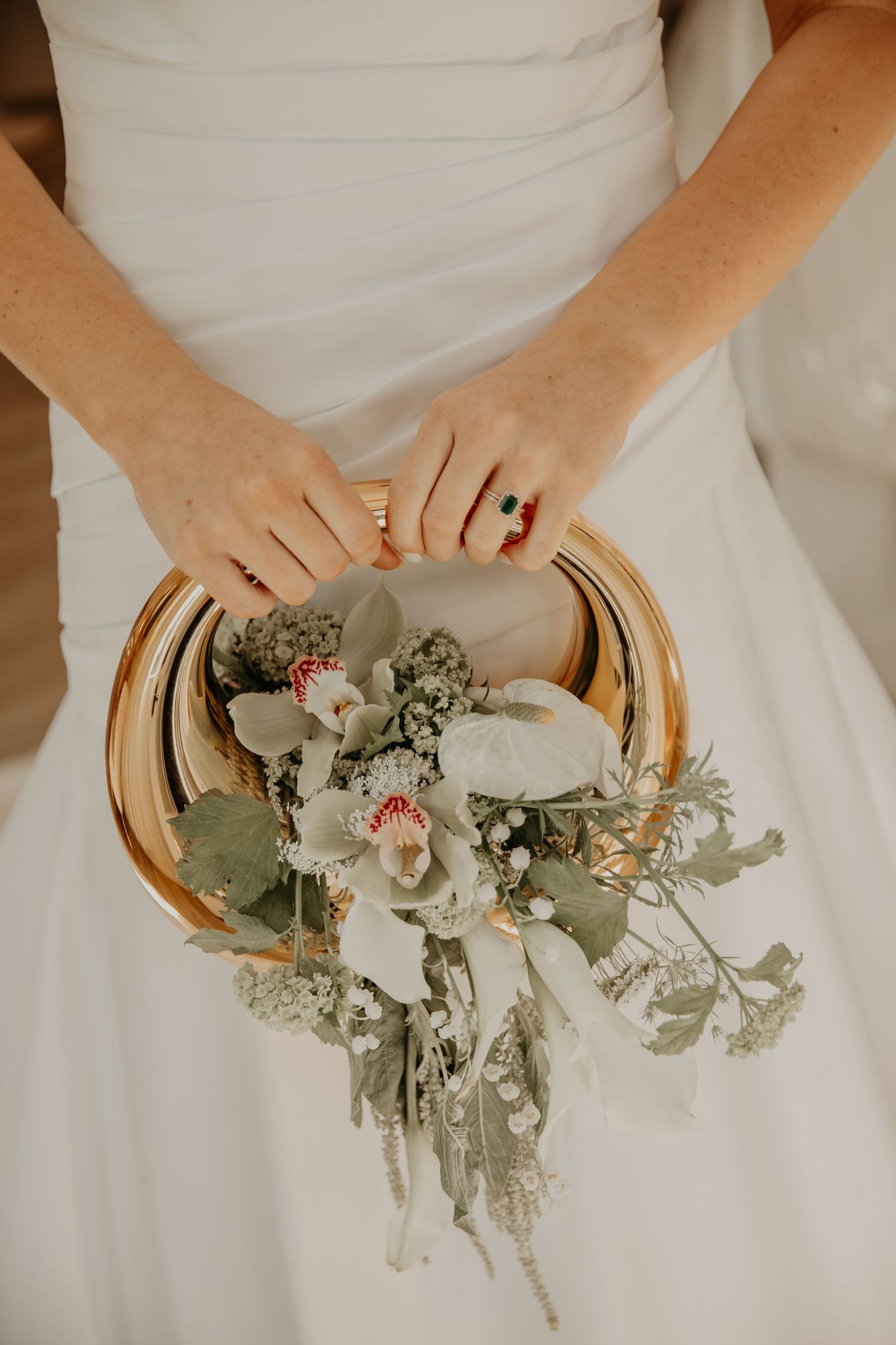 Close-up of wedding bouquet with white orchids and eucalyptus held against a white dress.