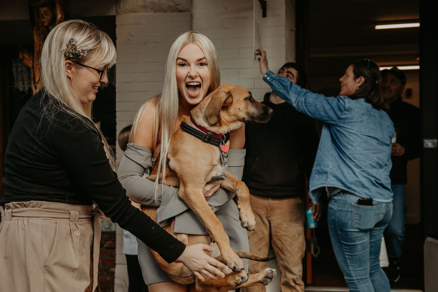 Three people share a joyful moment playing with a happy golden retriever dog indoors.
