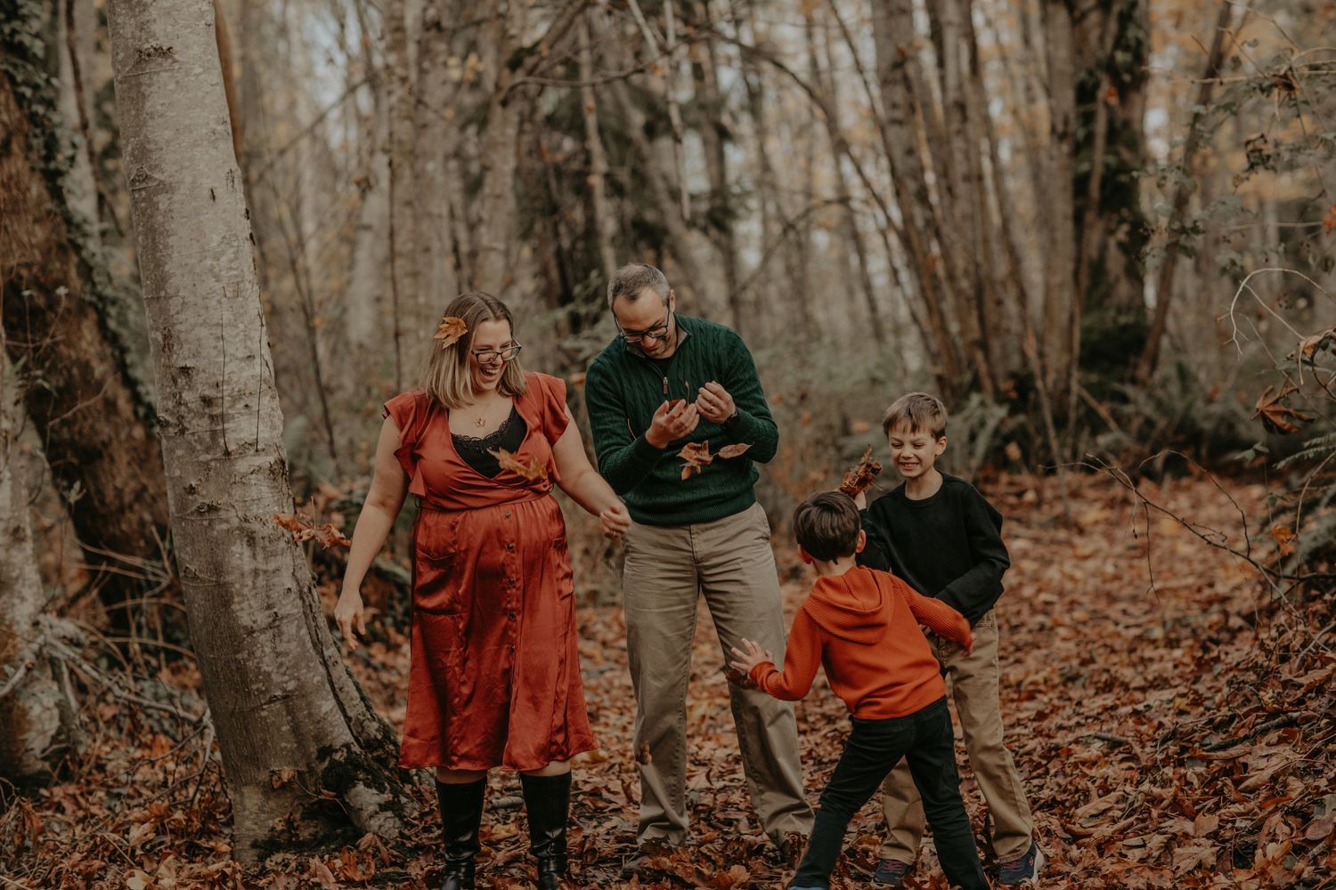Family enjoying a playful moment together while walking through a misty autumn forest with fallen leaves.