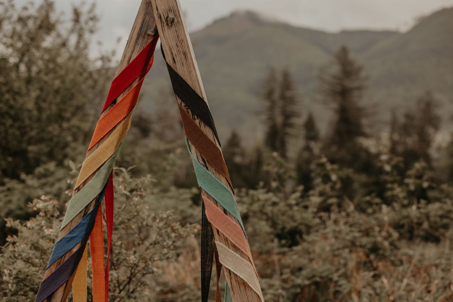 Colorful feathers tied to wooden poles against a misty mountainous backdrop with evergreen trees.