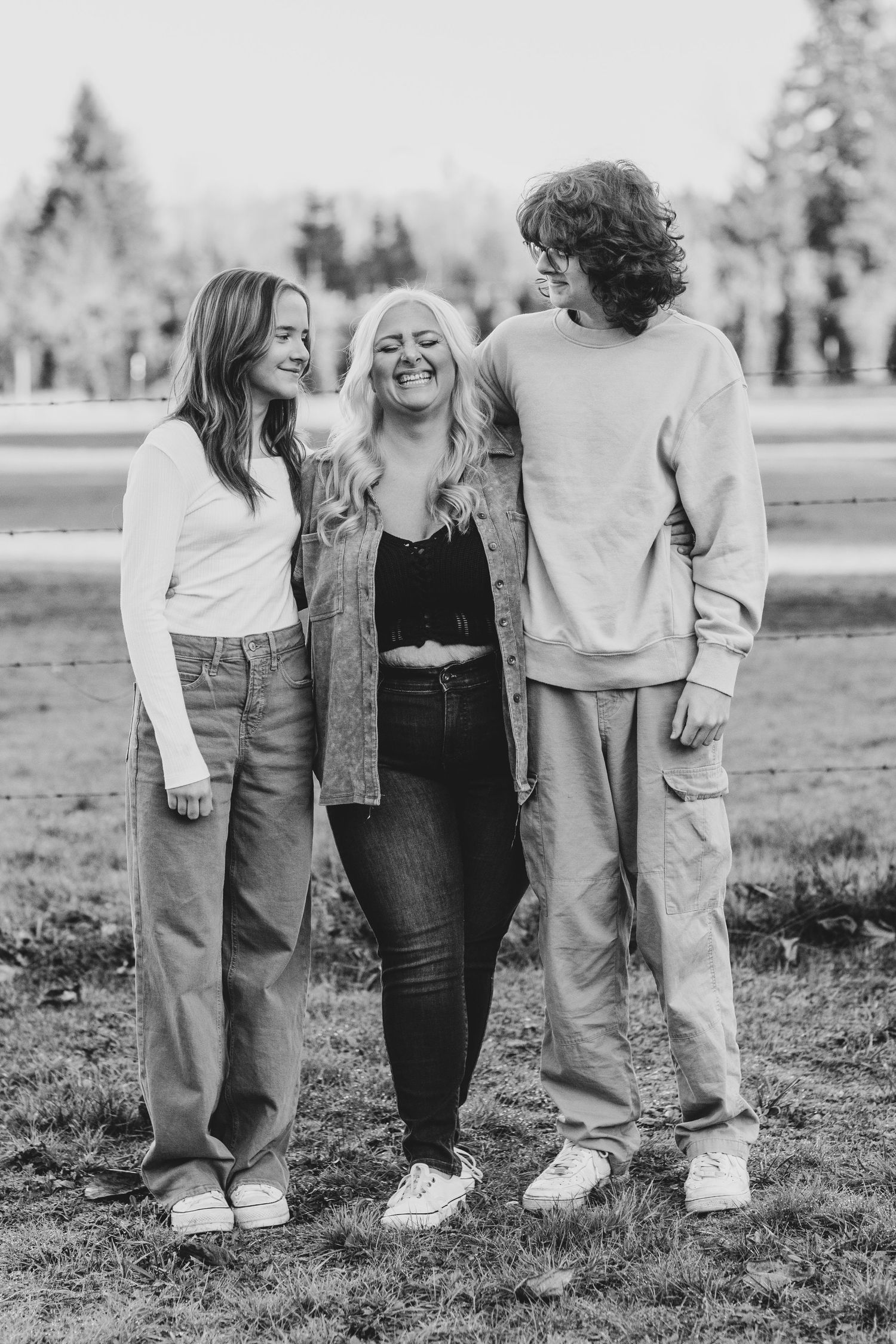 A black and white portrait of three friends standing together outdoors in casual clothing on a grassy field.