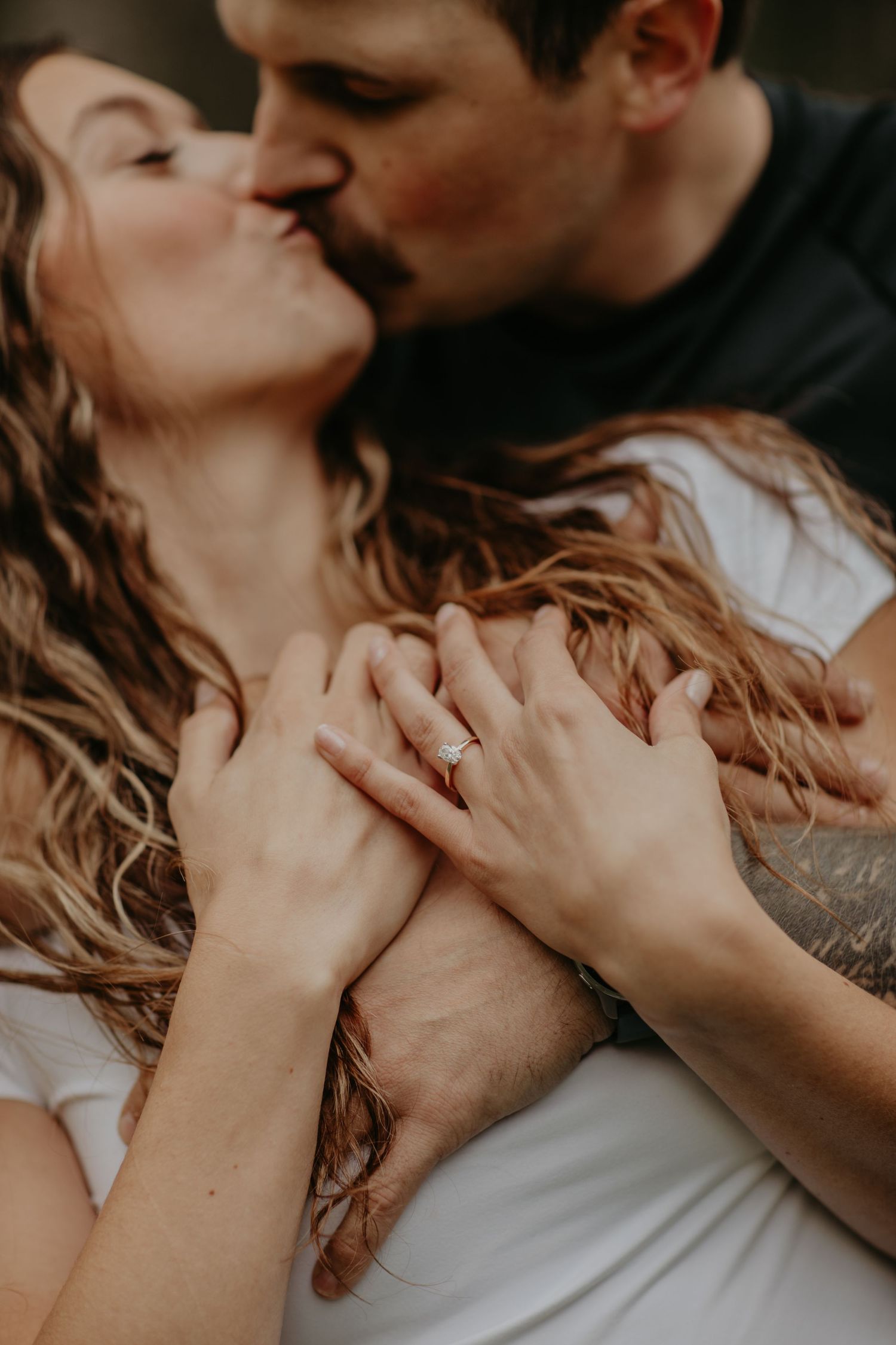 Intimate romantic moment with hands clasped together and flowing blonde hair in moody lighting.