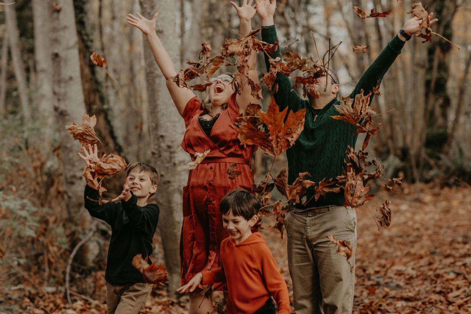 A group enjoying an autumn day in the woods throwing colorful fallen leaves in the air.