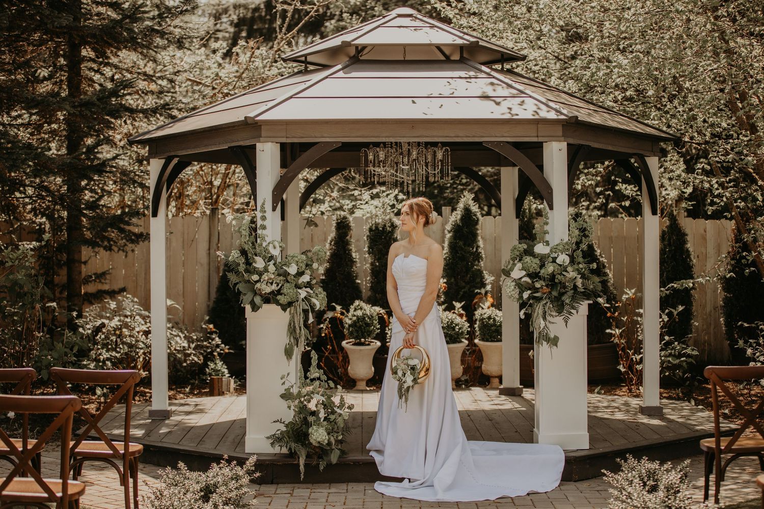 A beautiful white gazebo decorated with greenery and floral arrangements in an outdoor garden wedding setting.