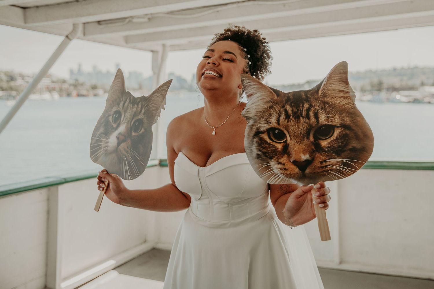 Two adorable cats with large expressive faces pose on a white boat deck with someone in a white dress.