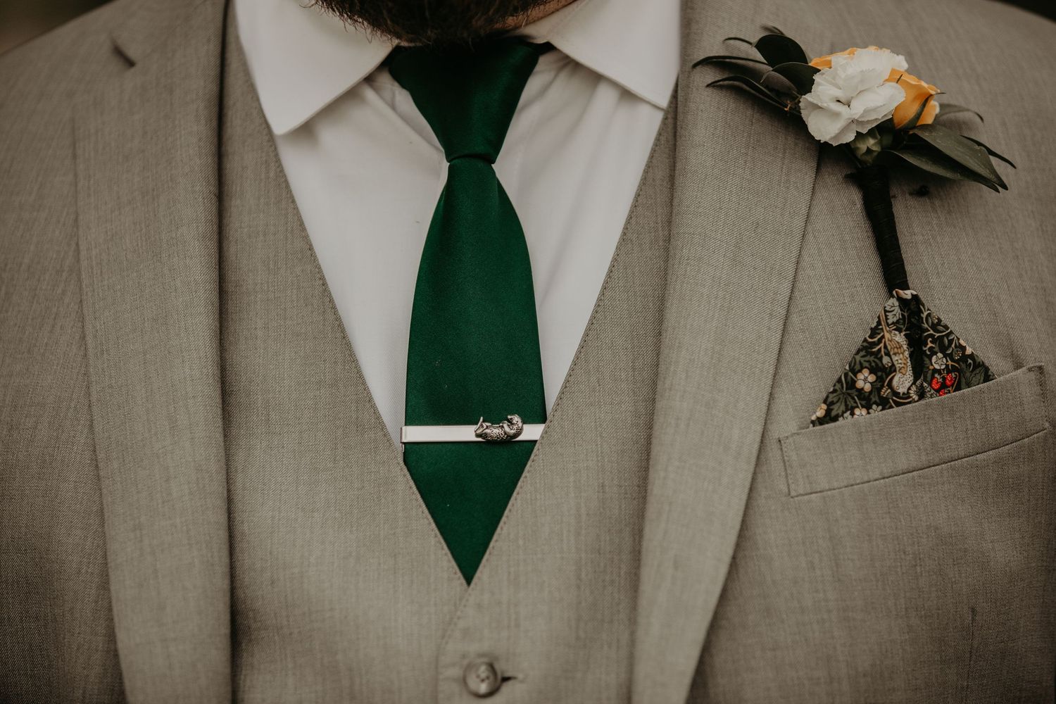 Close-up detail of gray suit with emerald green tie and floral boutonniere.