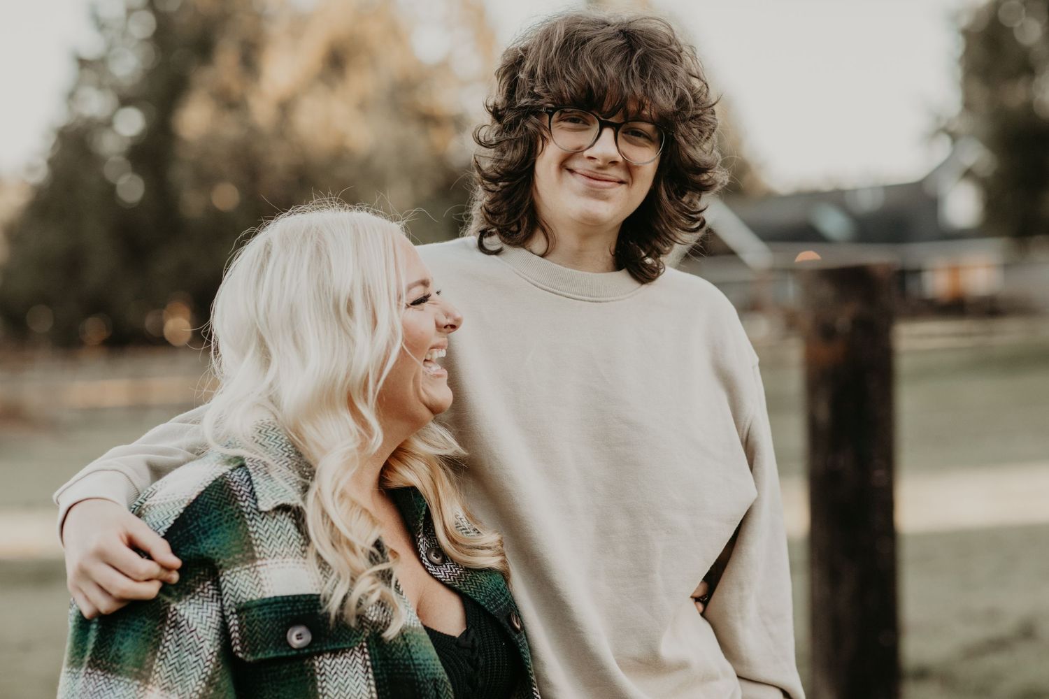 Two smiling friends laugh together while embracing outdoors during a warm autumn day.