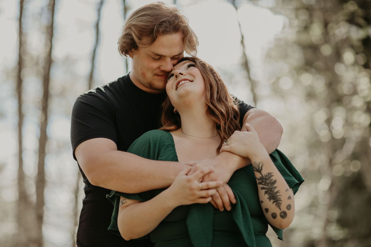 Couple embraces tenderly in warm sunlight filtering through forest trees during intimate outdoor photo session.