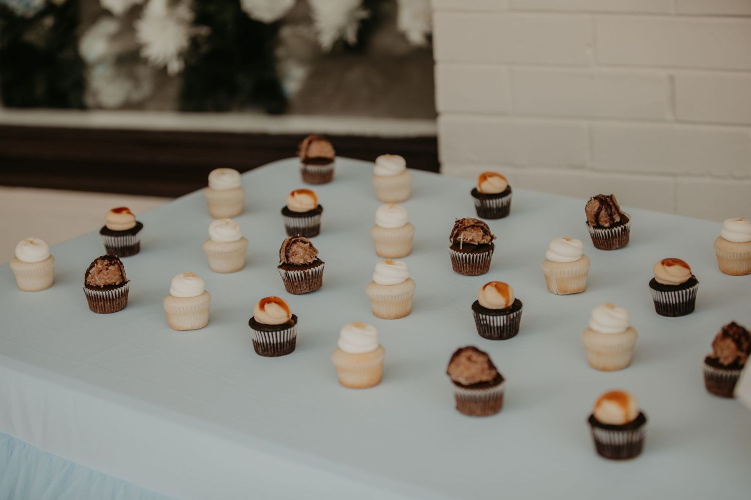 Chocolate and vanilla mini cupcakes arranged in a scattered pattern on a light blue tablecloth.