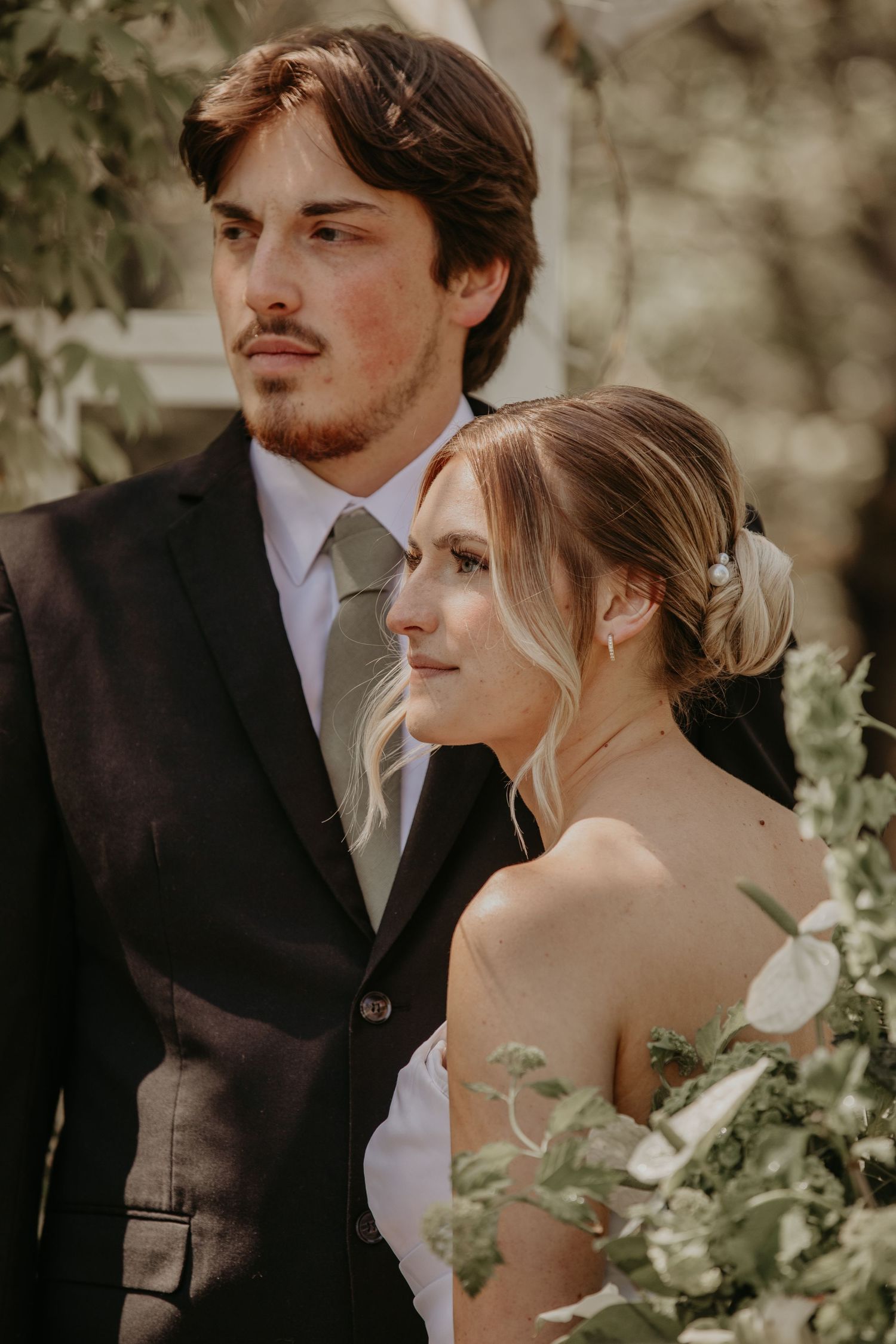 A fine art wedding portrait with the couple posing in elegant attire among lush greenery with vintage warm tones.