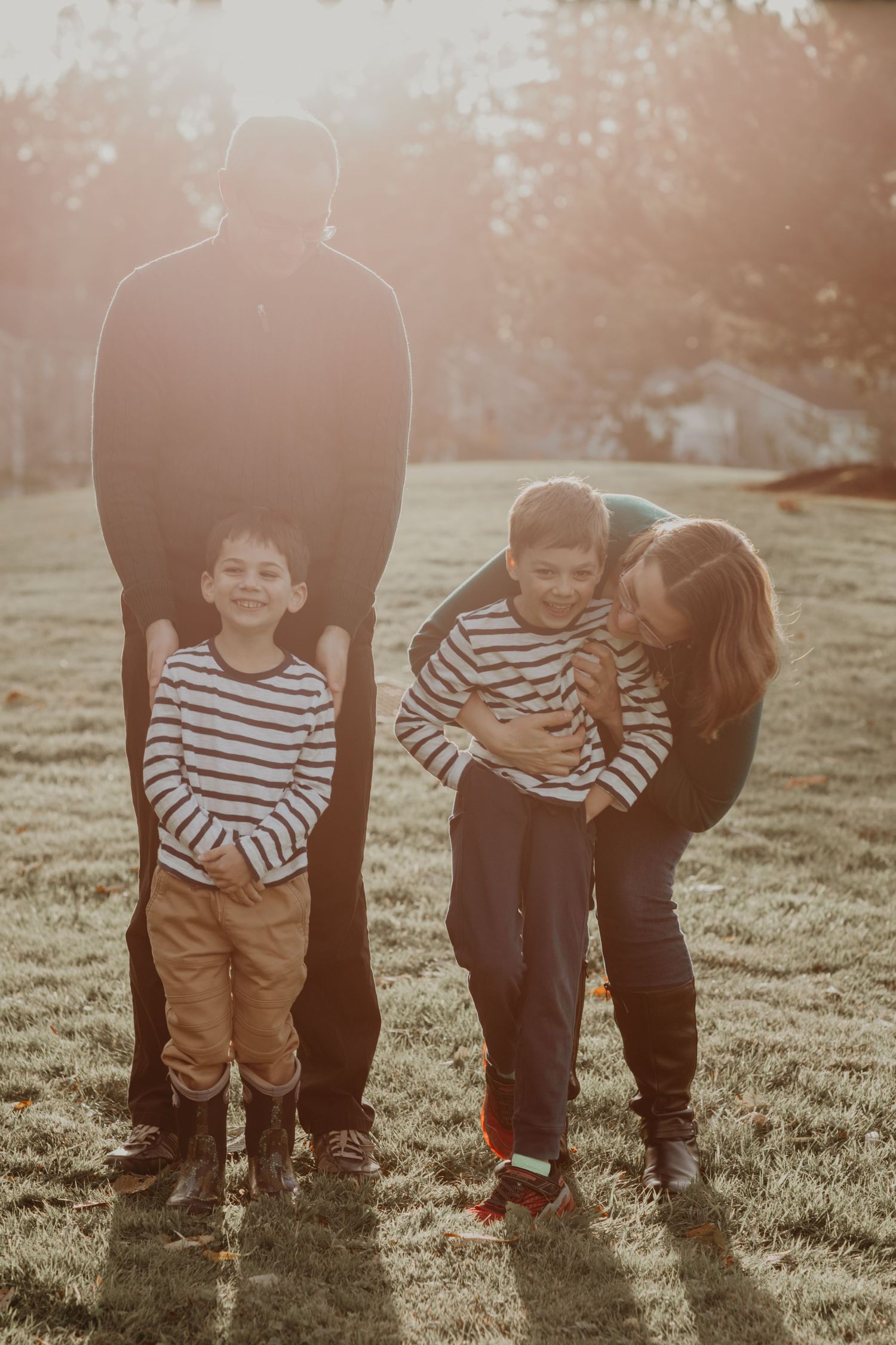 A family wearing striped shirts stands together in a grassy field during golden hour sunset.