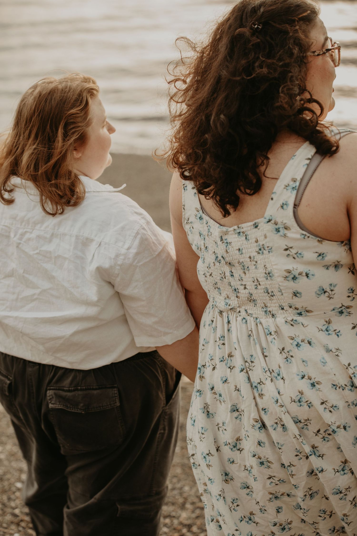 Two people in casual attire standing together outdoors, one wearing a floral dress and one in a white shirt.