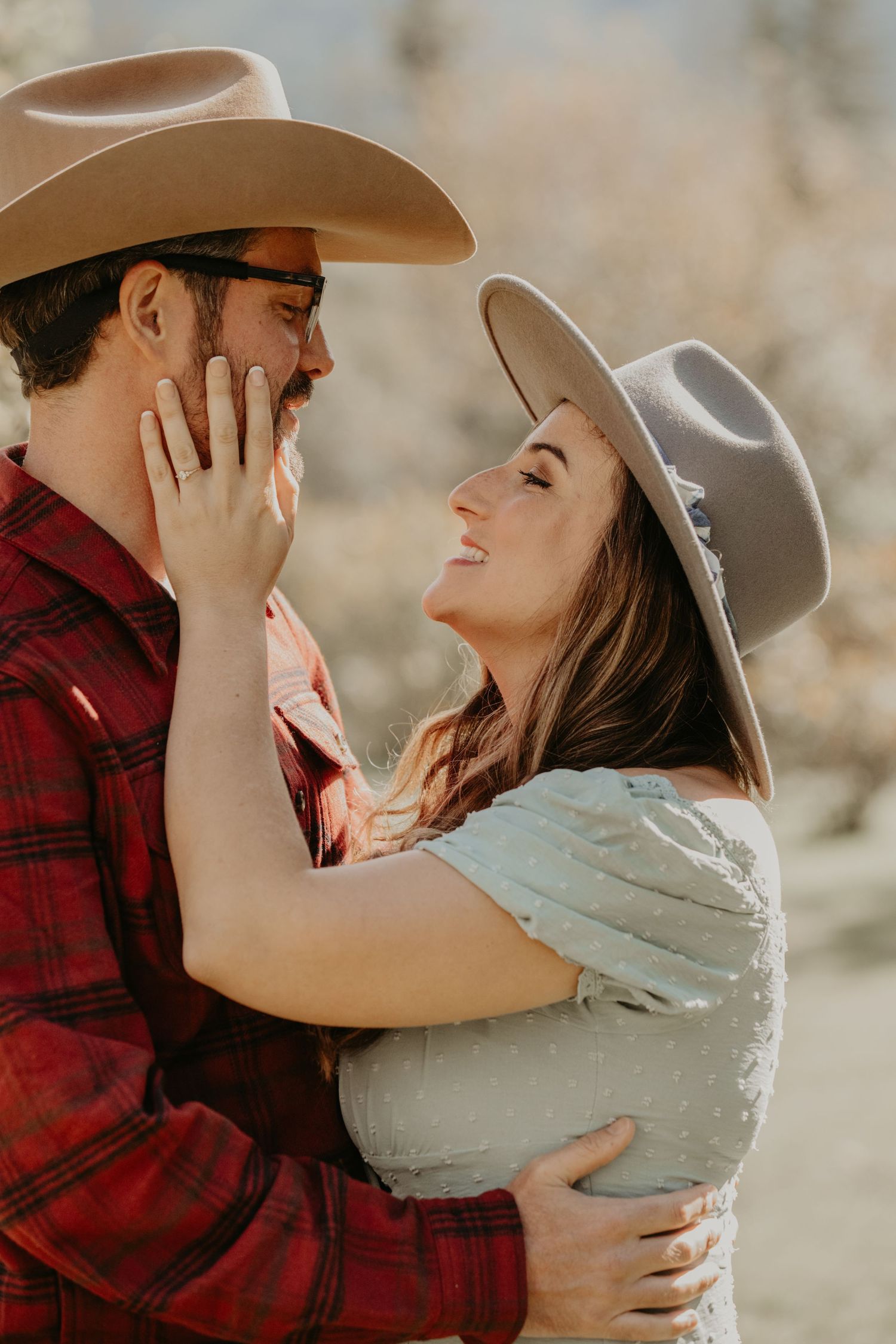 Two cowboys in love share an intimate moment outdoors wearing cowboy hats and western attire.