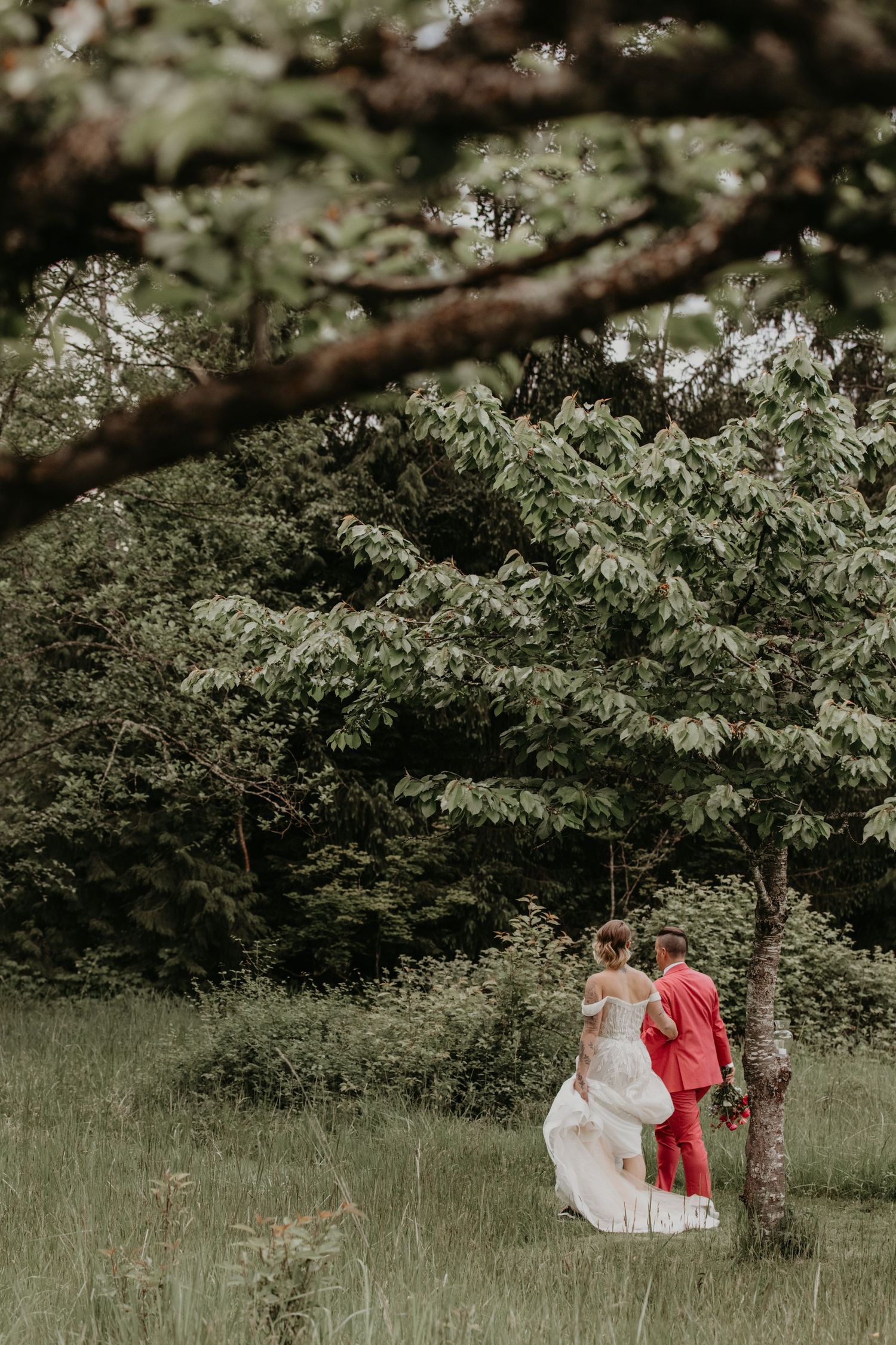 Couple stands together among lush trees and greenery in a romantic outdoor wedding setting.