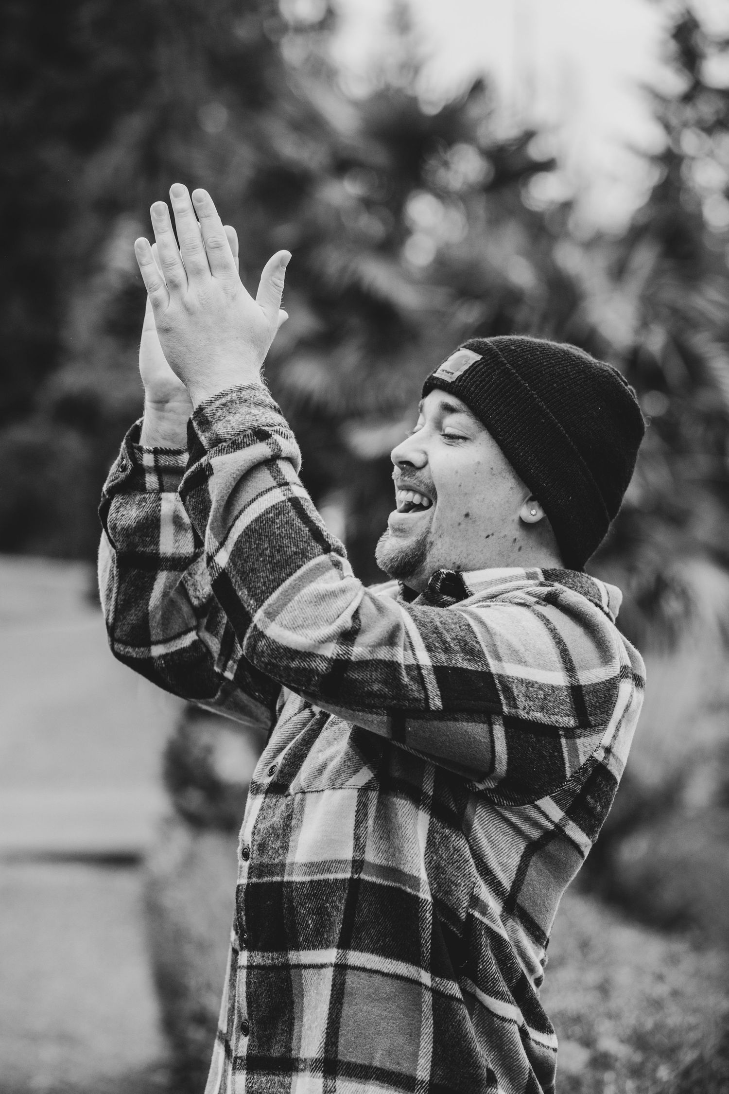 Black and white photo of a joyful person in a plaid flannel shirt and beanie raising their hands in celebration.