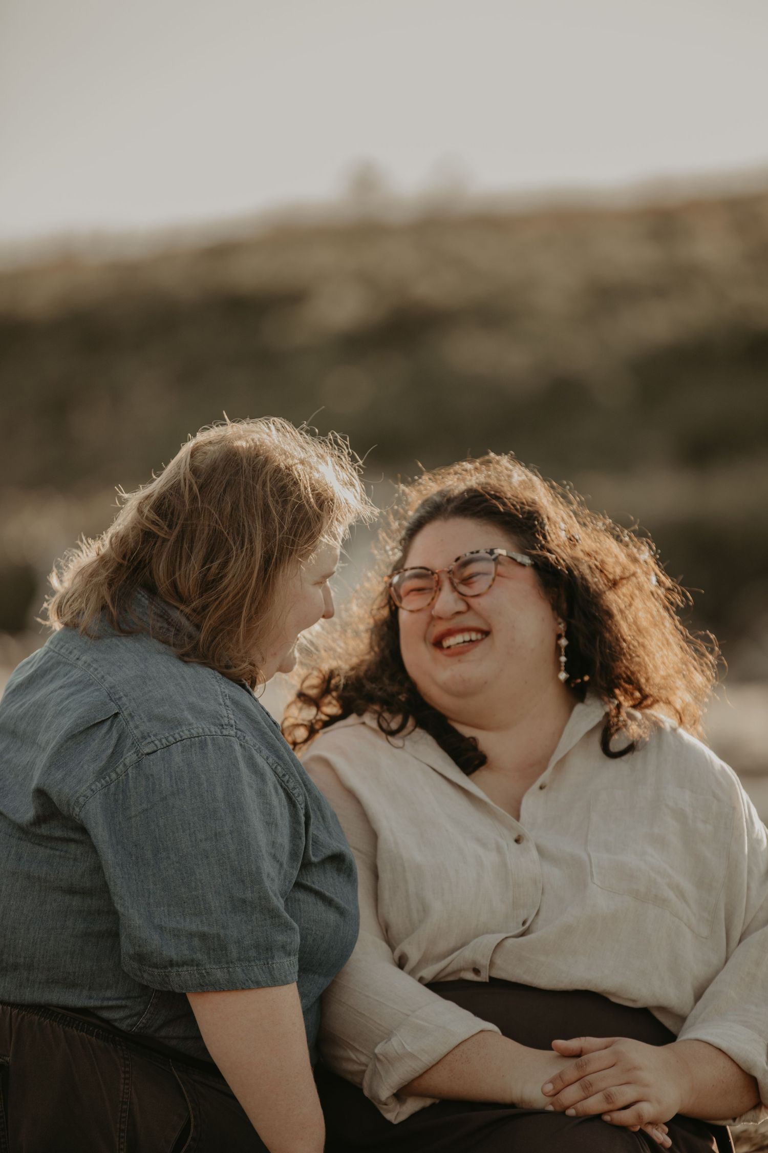Two people sitting outdoors sharing a joyful laughing moment together at sunset in casual attire.