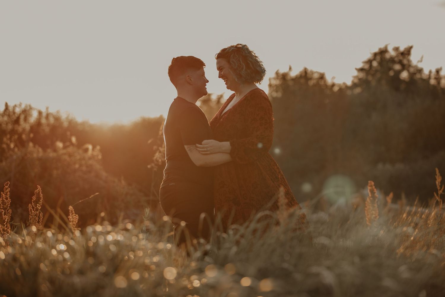 A romantic couple stands silhouetted against a golden sunset in a dreamy outdoor setting.