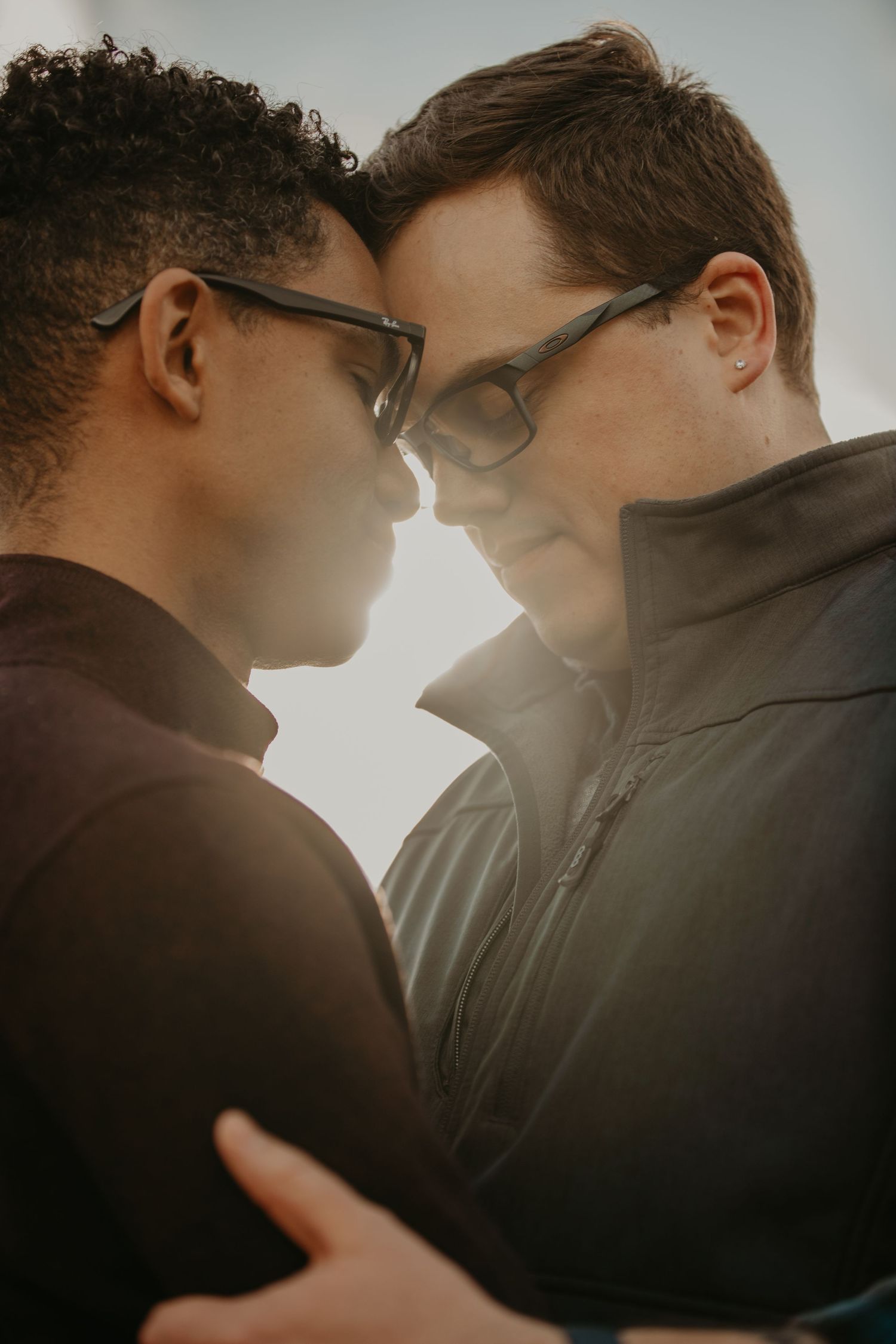 A couple in glasses sharing an intimate moment together against a glowing sunset background.