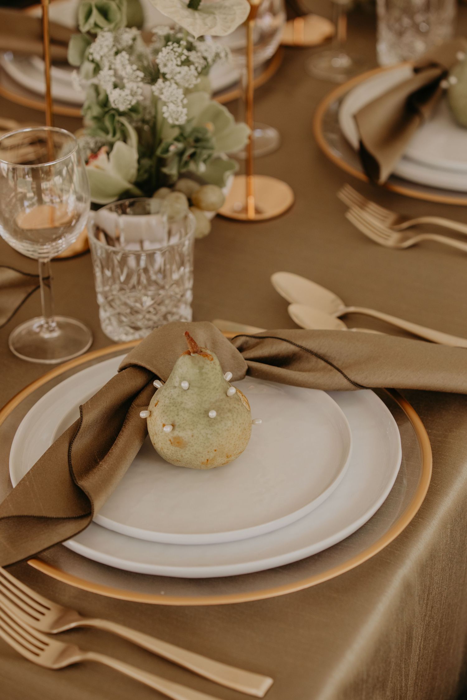 Elegant table setting with gold charger plates, white dishes, linen napkins, crystal glasses and delicate floral centerpiece.